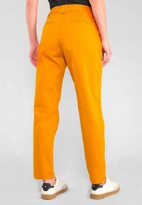 Helle orange Hosen mit einem geraden Bein, aus Baumwollmaterial, mit Gesäßtaschen und einer glatten Textur, kombiniert mit weißen Sneakers.