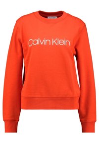 Oranžová mikina s dlouhými rukávy, žebrovanými manžetami a lemem. Na přední straně je bílý nápis "Calvin Klein". Měkká, hladká tkanina.