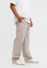 Béžové rovné nohavice s bočnými vreckami, vyrobené z ľahkej látky. Nosené s bielym tričkom a krémovými teniskami s jemnými akcentmi.