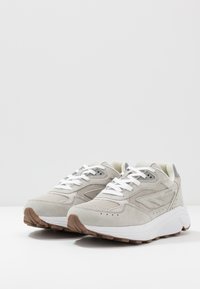 Lys grå sneakers med en blanding af ruskind og mesh-materialer. Har hvide snørebånd, perforerede detaljer og en tekstureret gummisål.