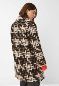 Wollen blend jas met een geometrisch patroon in bruin, crème en zwart. Het heeft een brede kraag en oranje accenten op de mouwen.