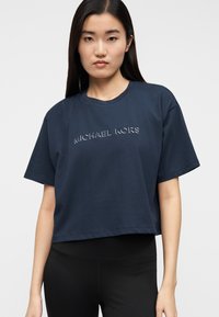 T-shirt azul-marinho cropped em algodão, com mangas curtas e logótipo em relevo ao centro. Textura suave, design minimalista.