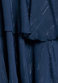 Donkerblauwe jurk met een vloeiende ontwerp, subtiele textuur en glinsterende metallic draden, die een gelaagd effect creëren.