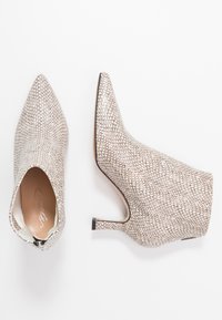 Pointed-toe ankle boots in a textured, metallic silver finish. Features a sleek silhouette and a small, black heel. Zipper closure at the back.