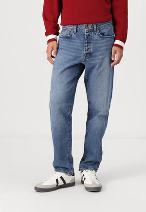 Denim jeans in light blue with a straight-leg cut, five-pocket design, and a button and zipper closure. Worn with white sneakers.