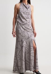 Halter-neck evening gown in light gray satin with black floral pattern, featuring a side slit and flowing design. Smooth texture.