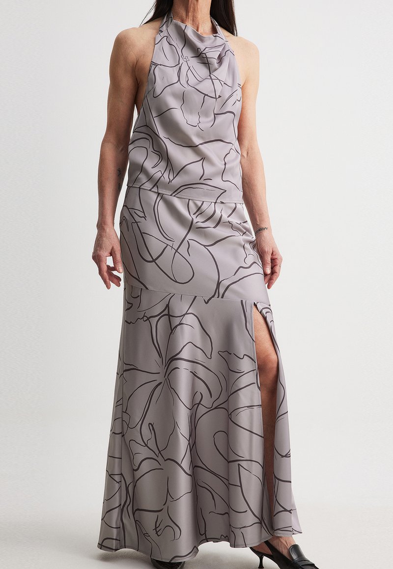 Halter-neck evening gown in light gray satin with black floral pattern, featuring a side slit and flowing design. Smooth texture.