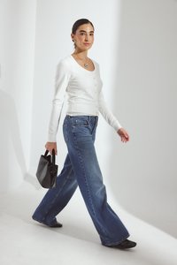 Valkoinen pitkähihaisten napillinen paita yhdistettynä leveisiin sinisiin farkkuihin ja mustiin teräväkärkisiin kenkiin, pitäen pientä mustaa käsilaukkua.