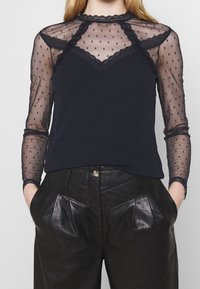 Marinblus med genomskinliga ärmar av prickig nät, spetsdetalj vid halsringningen, mjukt tyg, tillsammans med högmidjade svarta läderbyxor.