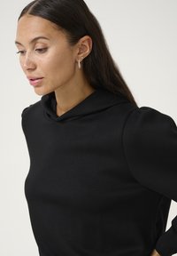 Černá mikina s vysokým límcem, jemná textura a nabírané rukávy. Ve spojení se stříbrnými náušnicemi, které mají minimalistický design.