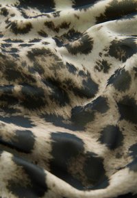Tissu lisse avec motif léopard noir et beige, montrant des plis et des détails de texture.