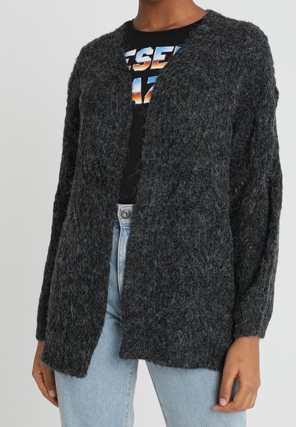 Cardigan gris foncé en matière pelucheuse, ouvert sur le devant, porté par-dessus un t-shirt noir à motif et un jean taille haute bleu clair.