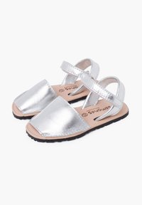 Silberne metallische Sandalen mit quadratischen Zehen, zwei verstellbaren Riemen und einer schwarzen Gummisohle. Sichtbare Leder-Innensohle mit Markenlogo.