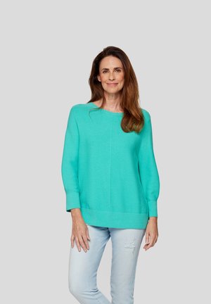 Türkiser Pullover mit langen Ärmeln, lockerer Passform und gerippten Bündchen. Kombiniert mit hellblauen, ausgefransten Jeans. Glatte, weiche Textur.