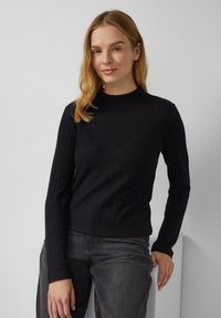 Czarna pr ążkowana bluzka z długim rękawem i wysokim kołnierzem. Materiał wydaje się miękki i teksturowany, dopasowany krój podkreśla sylwetkę.