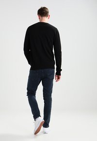 Zwarte trui met een ronde hals, gecombineerd met donkerblauwe slim-fit jeans en witte sneakers, gezien vanaf de achterkant.