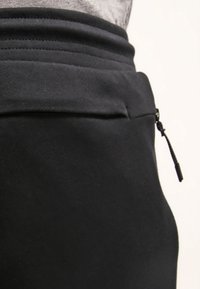 Black jogger pants with a textured fabric, featuring a wide elastic waistband and a side zipper pocket.