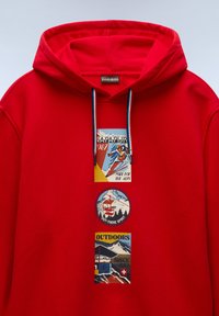 Felpa rossa con cappuccio e cordoncino, caratterizzata da tre toppe grafiche: design vintage di sci e un logo circolare con immagini di montagne. Texture morbida.