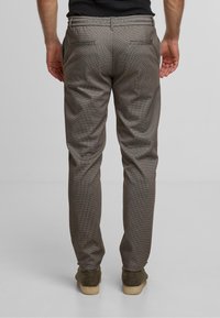 Brune ternede bukser med en skræddersyet pasform, flad front og to baglommer. Båret med strukturerede grønne sko.