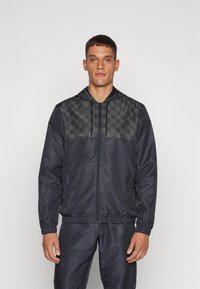 Chaqueta de punto navy con un patrón de tablero de ajedrez en la parte superior del pecho, dos bolsillos laterales y capucha. Fabricada con un tejido ligero y suave.