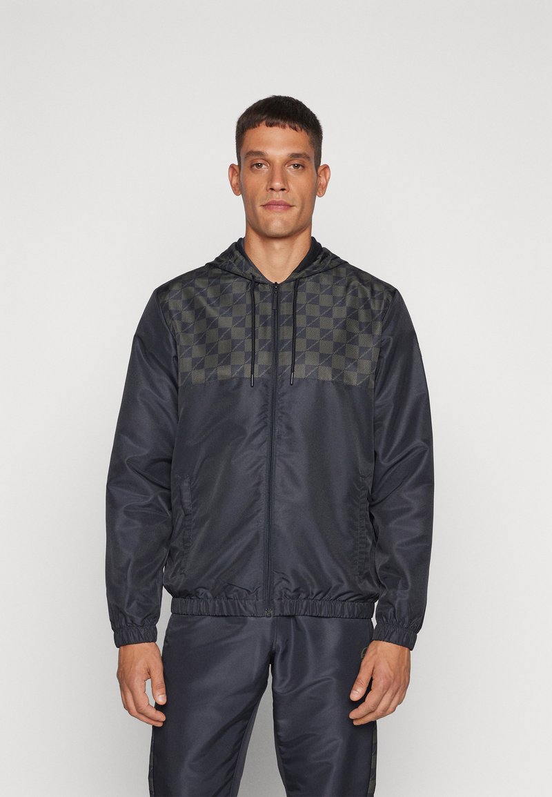 Chaqueta de punto navy con un patrón de tablero de ajedrez en la parte superior del pecho, dos bolsillos laterales y capucha. Fabricada con un tejido ligero y suave.