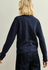 Maglione lavorato a maglia blu navy con finitura testurizzata, scollo rotondo, maniche lunghe e orlo a coste, abbinato a jeans in denim scuri.