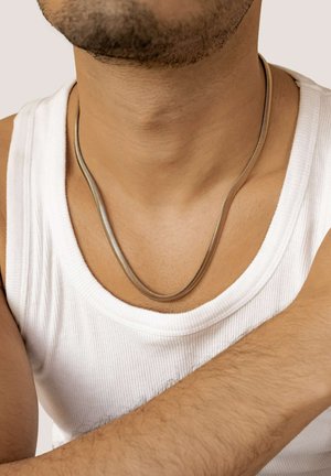 Silberne Metallkette mit einem glatten, geschwungenen Design, die auf der Haut liegt und mit einem weißen, gerippten Tanktop kombiniert ist.