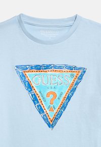 Ανοιχτό μπλε μπλουζάκι με πολύχρωμο τρίγωνο λογότυπο Guess που περιλαμβάνει το κείμενο "GUESS U.S.A." και ένα πορτοκαλί ερωτηματικό στο κέντρο.