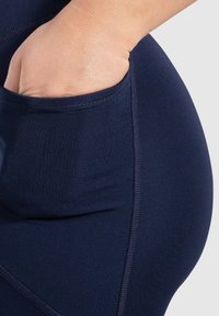 Leggings sportivi blu navy con un design aderente, dotati di una tasca laterale e realizzati in tessuto morbido e elastico con cuciture rinforzate.