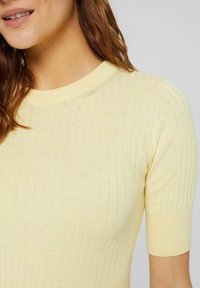 Short-sleeve, ribbed-knit top in pale yellow. Soft texture with a round neckline and fitted design highlighting body contours.
