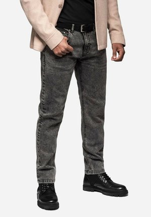 Jeans en denim gris avec une coupe slim, présentant un design classique à cinq poches, associés à des bottes noires à lacets et à une chemise noire.