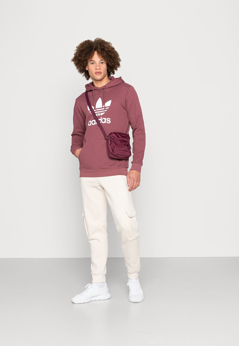 Bordo kapuką su baltu logotipu, smėlio spalvos kargo pusiau kelnių ir baltų sportbačių derinys. Outfit'as papildytas maža bordo rankine per petį.