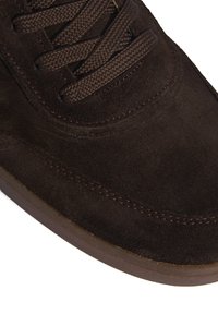 Baskets en daim marron avec des lacets ronds, un col rembourré et des accents cousus sur le dessus, dotées d'une semelle en caoutchouc texturée.