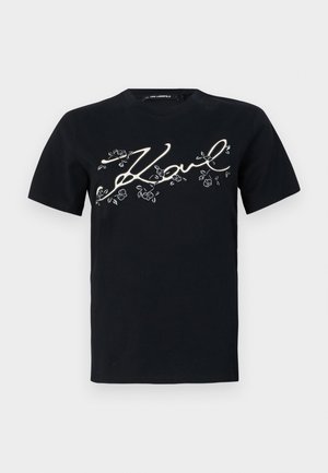 Black cotton t-shirt featuring a printed white “Karl” signature design with floral accents. Short sleeves and a standard crew neckline.