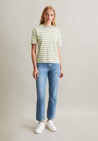 T-shirt rayé vert et blanc, à manches courtes, col rond, associé à un jean droit bleu clair et des baskets blanches. Design simple, look décontracté.