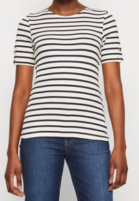 Randig kortärmad topp med marinblå och vit ribbad tyg; har knäppte detaljer på ärmarna, rund halsringning och en figurnära design.