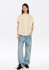 Yellow short-sleeve button-up shirt with a textured pattern, paired with light blue wide-legged jeans and black sneakers.