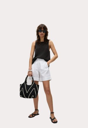 Zwart mouwloos topje, witte linnen shorts, zwarte sandalen, met een gestructureerde zwarte tas met wit zigzagpatroon, weergegeven tegen een lichte achtergrond.