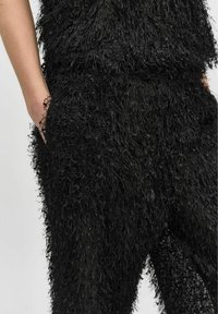 Zwart textuuroutfit met een fluffy, rafelige stof en een losse pasvorm. Kenmerken zijn onder andere zakken en een algehele zachte, gelaagde uitstraling.