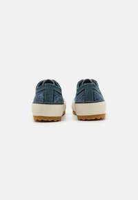 Sapatos casuais em camurça azul com uma sola de borracha de cor creme, apresentando um calcanhar texturizado e costuras visíveis no painel traseiro.