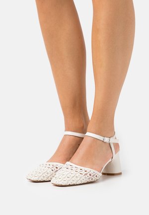 Sandales à talons blancs avec un empiècement textile tissé, bout ouvert et bride à la cheville. Le talon est épais, avec une finition lisse.