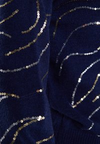 Marineblauer Stoff mit wellenförmigen Mustern aus goldenen und silbernen Pailletten. Weiche Textur mit gestricktem Aussehen, Nahaufnahme.
