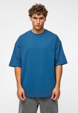 Blauw oversized t-shirt, korte mouwen, ronde hals, gemaakt van zachte katoen. Gekocht met grijze vervaagde jeans, minimalistisch ontwerp, zonder patronen of accenten.