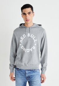 Šedá mikina s kapucí z měkkého materiálu, zdobená velkým bílým kruhovým designem s textem "RED BULL RACING". Elastické manžety a spodní lem, kapuce se stahovací šňůrkou.