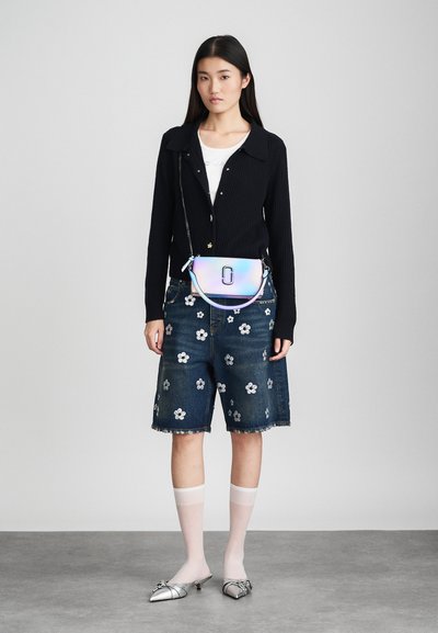 Cardigan a coste nera, camicia bianca, shorts in denim con applicazioni floreali, borsa a tracolla iridescente, calze trasparenti fino al ginocchio, mule argentati.