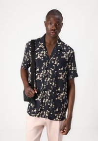 Navy short-sleeve shirt with a floral pattern in cream, featuring a camp collar, front buttons, and worn with light pink trousers.