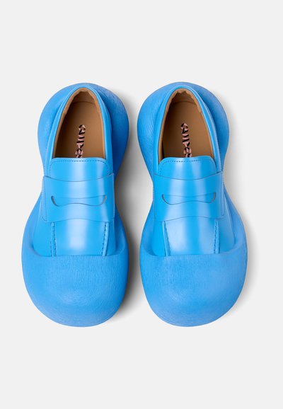 Scarpe slip-on blu realizzate con materiali lisci e testurizzati, caratterizzate da un design a profilo basso, punta arrotondata e una band decorativa prominente.