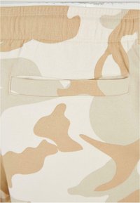 Shorts de camouflage beige avec une taille élastique, dotés d'une poche arrière et d'un tissu doux et texturé. Le motif varie en nuances de couleur.