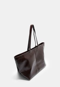 Dunkelbraune Ledertasche mit langen Tragegriffen, Nähdetails und einer glatten, leicht glänzenden Oberfläche, die auf einem hellen Hintergrund aufrecht steht.