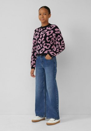 Pull noir en peluche avec imprimé léopard rose, associé à un jean bleu taille haute à jambes larges et des baskets blanches avec une semelle beige.